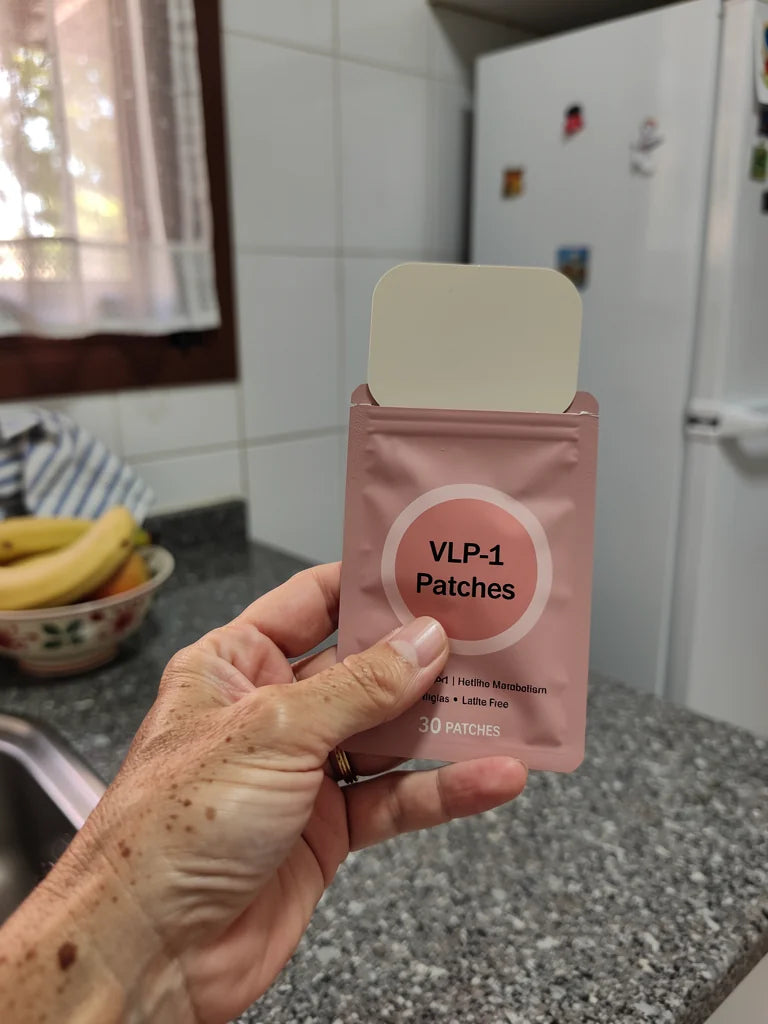 Mano sosteniendo el sobre rosa del parche VITA GLP-1 en una cocina espanola